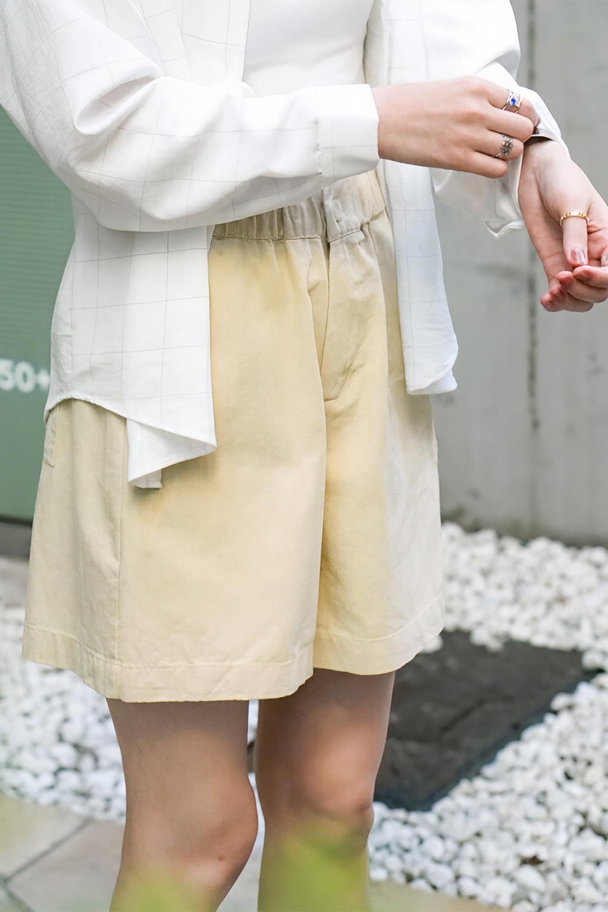Model wearing a white shirt and beige shorts standing on a gravel path.