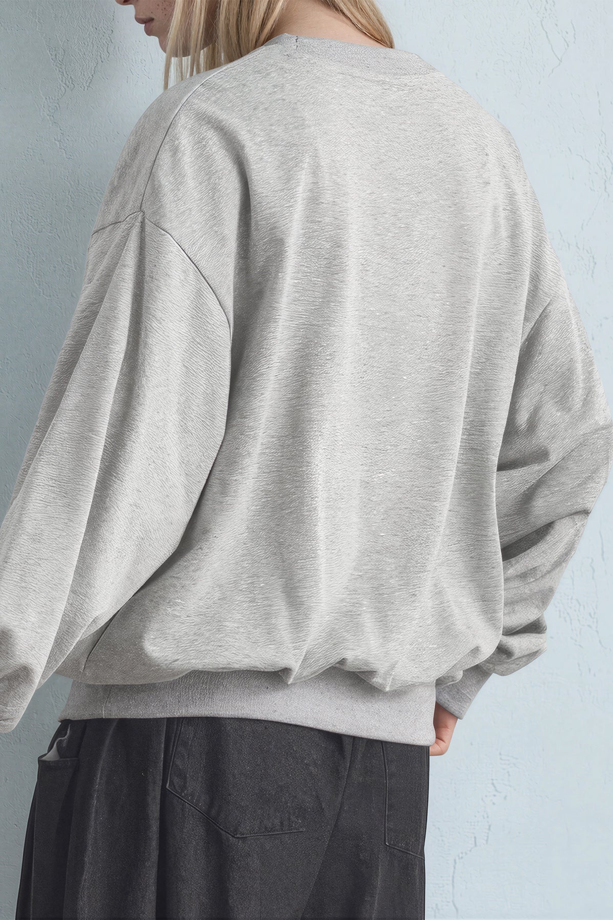 Person wearing a light gray oversized sweatshirt against a light blue wall.