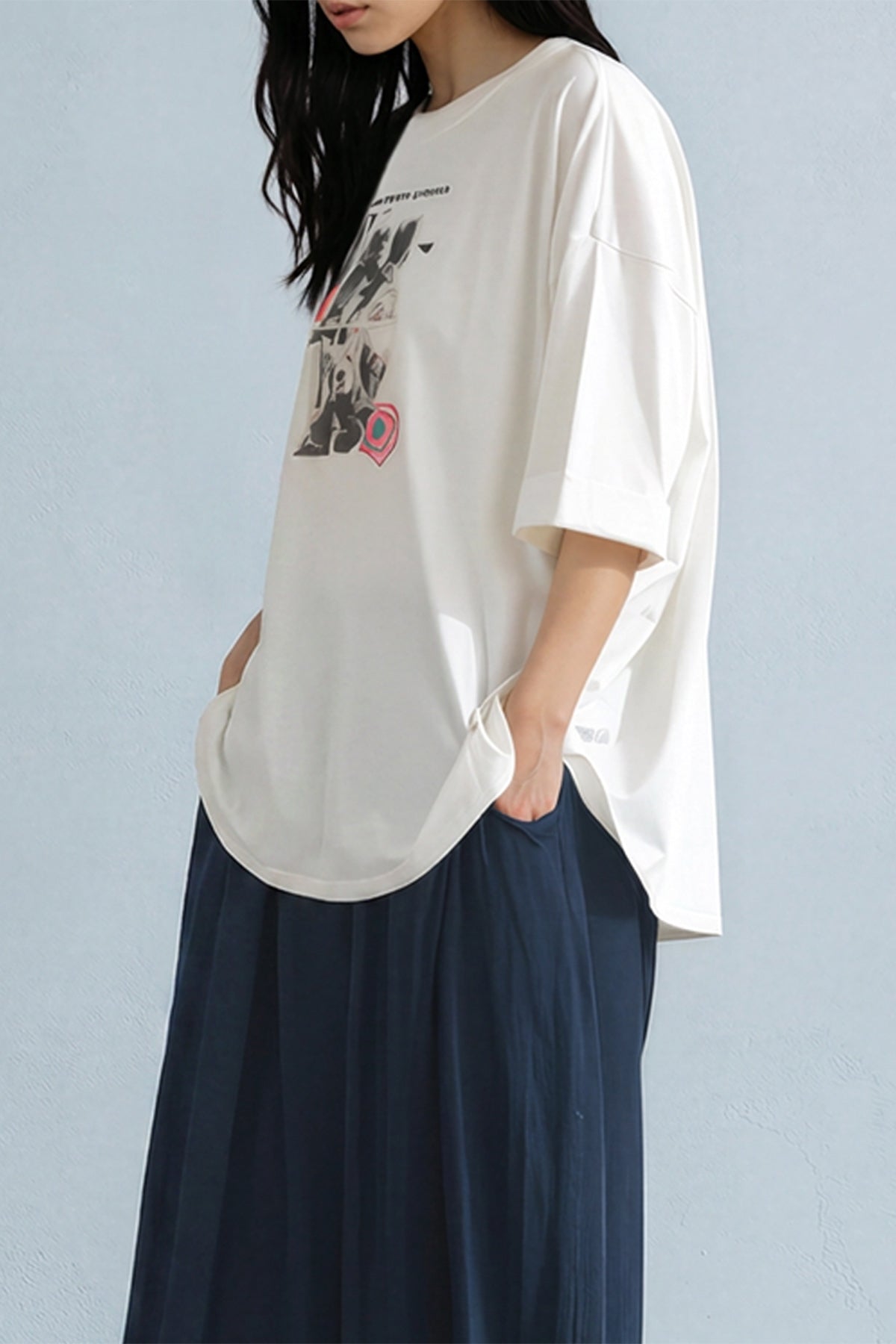 Person wearing a white oversized t-shirt with a graphic design and dark pants against a light blue background