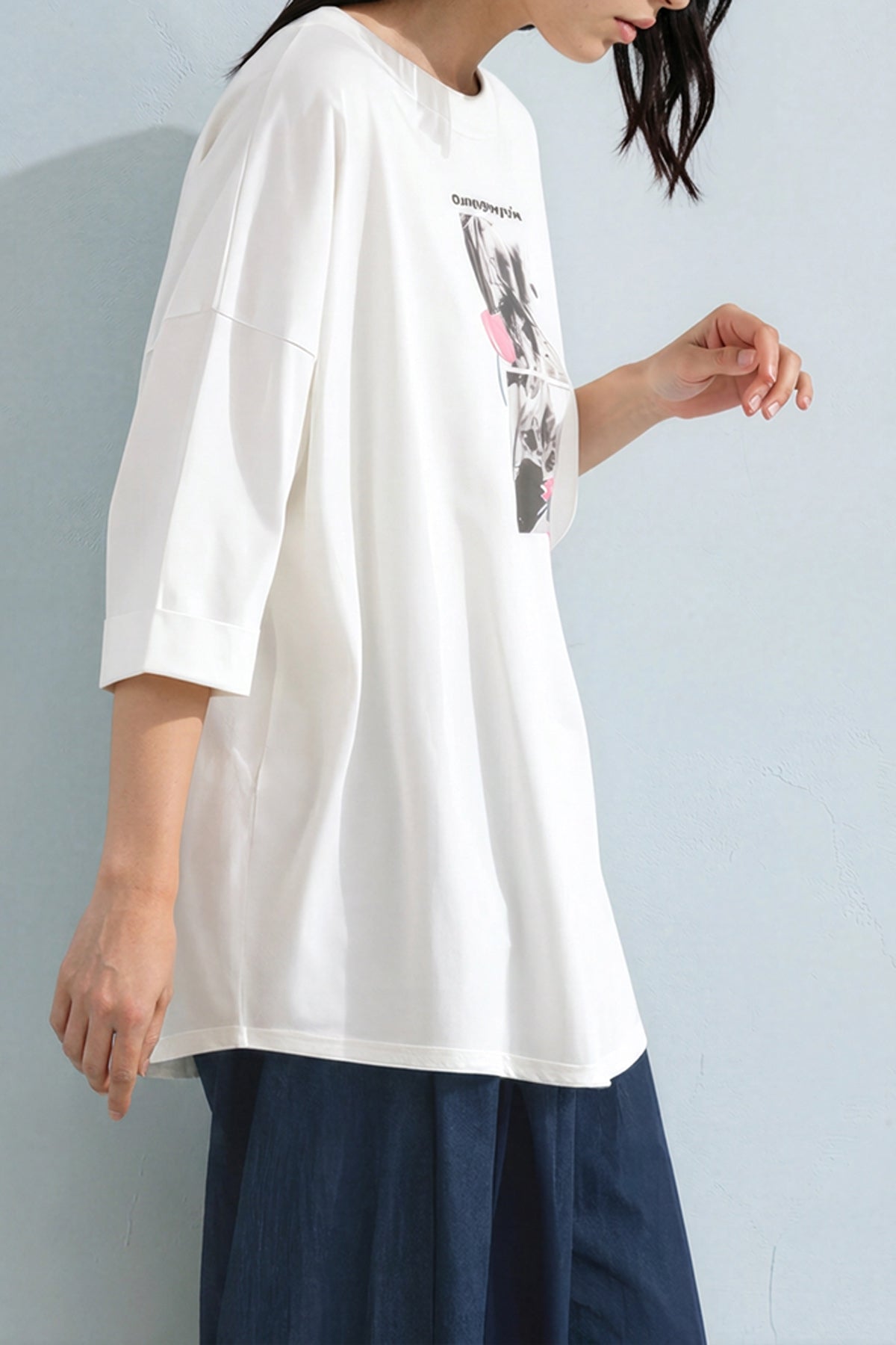 Person wearing a white oversized t-shirt with a graphic design on a plain background